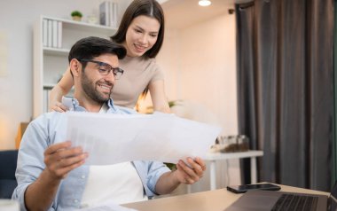 Evde kız arkadaşıyla bilgisayarla çalışırken gülümseyen genç bir serbest çalışanın portresi.