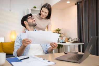 Evde kız arkadaşıyla bilgisayarla çalışırken gülümseyen genç bir serbest çalışanın portresi.