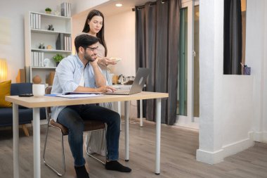 Evde kız arkadaşıyla bilgisayarla çalışırken gülümseyen genç bir serbest çalışanın portresi.