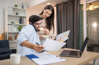 Evde kız arkadaşıyla bilgisayarla çalışırken gülümseyen genç bir serbest çalışanın portresi.