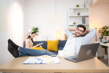 Evde kız arkadaşıyla bilgisayarla çalışırken gülümseyen genç bir serbest çalışanın portresi.