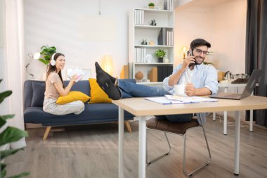 Evde kız arkadaşıyla bilgisayarla çalışırken gülümseyen genç bir serbest çalışanın portresi.