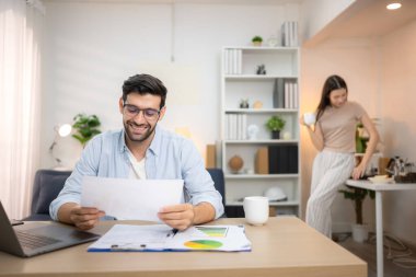 Evde kız arkadaşıyla bilgisayarla çalışırken gülümseyen genç bir serbest çalışanın portresi.