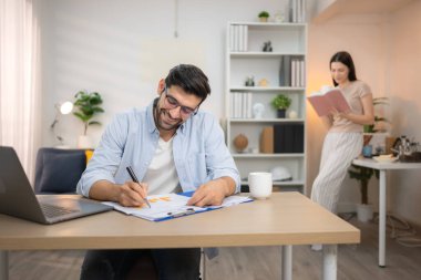 Evde kız arkadaşıyla bilgisayarla çalışırken gülümseyen genç bir serbest çalışanın portresi.