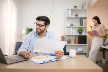 Evde kız arkadaşıyla bilgisayarla çalışırken gülümseyen genç bir serbest çalışanın portresi.