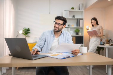 Evde kız arkadaşıyla bilgisayarla çalışırken gülümseyen genç bir serbest çalışanın portresi.