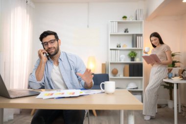 Evde kız arkadaşıyla bilgisayarla çalışırken gülümseyen genç bir serbest çalışanın portresi.