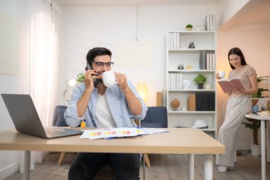 Evde kız arkadaşıyla bilgisayarla çalışırken gülümseyen genç bir serbest çalışanın portresi.