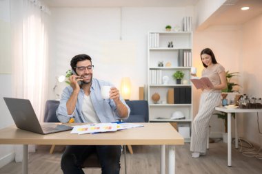 Evde kız arkadaşıyla bilgisayarla çalışırken gülümseyen genç bir serbest çalışanın portresi.