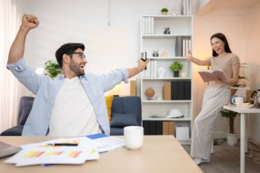 Evde kız arkadaşıyla bilgisayarla çalışırken gülümseyen genç bir serbest çalışanın portresi.