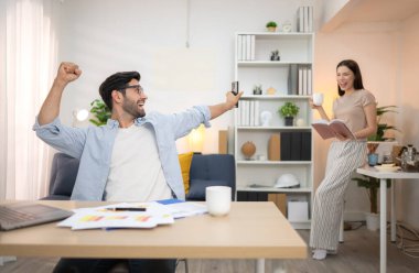 Evde kız arkadaşıyla bilgisayarla çalışırken gülümseyen genç bir serbest çalışanın portresi.