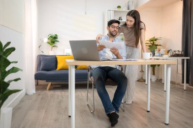 Evde kız arkadaşıyla bilgisayarla çalışırken gülümseyen genç bir serbest çalışanın portresi.