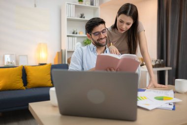 Evde kız arkadaşıyla bilgisayarla çalışırken gülümseyen genç bir serbest çalışanın portresi.