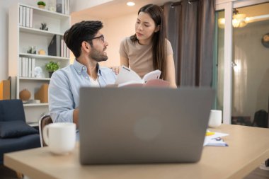 Evde kız arkadaşıyla bilgisayarla çalışırken gülümseyen genç bir serbest çalışanın portresi.