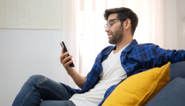 Akıllı telefon kullanan ve evdeki oturma odasında eğlenen genç bir serbest çalışanın portresi.