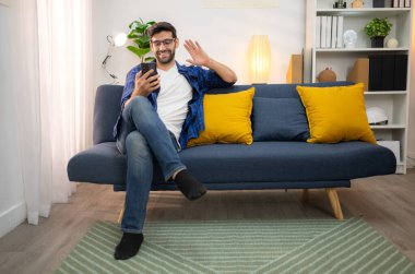 Akıllı telefon kullanan ve evdeki oturma odasında eğlenen genç bir serbest çalışanın portresi.