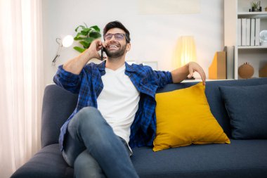 Akıllı telefon kullanan ve evdeki oturma odasında eğlenen genç bir serbest çalışanın portresi.