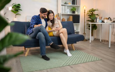 Genç çift rahatlarken gülümsüyor ve evdeki oturma odasında dizüstü bilgisayarla çalışıyorlar.