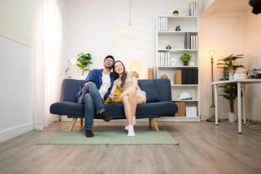 Genç çift rahatlarken gülümsüyor ve evdeki oturma odasında dizüstü bilgisayarla çalışıyorlar.