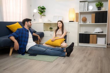 Genç çift rahatlarken gülümsüyor ve evdeki oturma odasında dizüstü bilgisayarla çalışıyorlar.