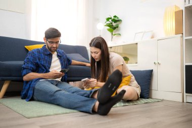 Genç çift rahatlarken gülümsüyor ve evdeki oturma odasında dizüstü bilgisayarla çalışıyorlar.