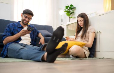 Genç çift rahatlarken gülümsüyor ve evdeki oturma odasında dizüstü bilgisayarla çalışıyorlar.