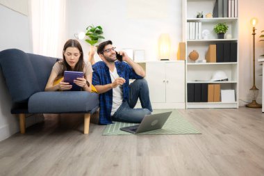 Genç çift rahatlarken gülümsüyor ve evdeki oturma odasında dizüstü bilgisayarla çalışıyorlar.