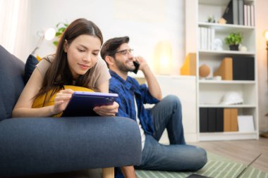 Genç çift rahatlarken gülümsüyor ve evdeki oturma odasında dizüstü bilgisayarla çalışıyorlar.