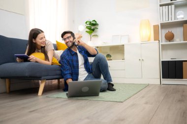 Genç çift rahatlarken gülümsüyor ve evdeki oturma odasında dizüstü bilgisayarla çalışıyorlar.