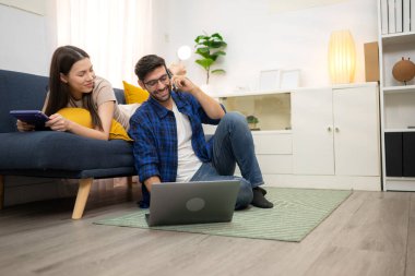 Genç çift rahatlarken gülümsüyor ve evdeki oturma odasında dizüstü bilgisayarla çalışıyorlar.