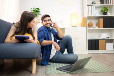 Genç çift rahatlarken gülümsüyor ve evdeki oturma odasında dizüstü bilgisayarla çalışıyorlar.