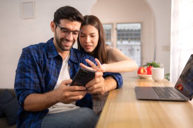 Evde kız arkadaşıyla bilgisayarla çalışırken gülümseyen genç bir serbest çalışanın portresi.