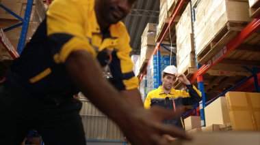 İki depo işçisi bir depodaki rafta saklamak için bir palet krikosunun üzerinde kutu dolusu mal taşıyorlar.