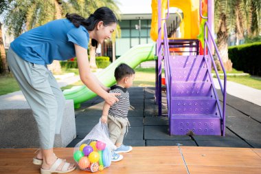Evde tatildeyken, bir anne parkta küçük bir çocukla bir şeyler yapıyor.