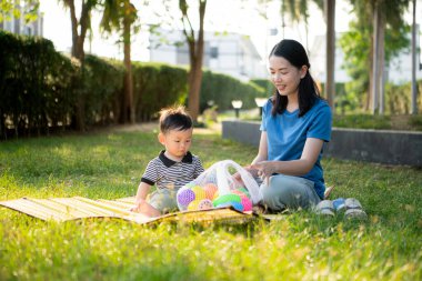 Evde tatildeyken, bir anne parkta küçük bir çocukla bir şeyler yapıyor.