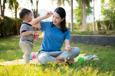 Evde tatildeyken, bir anne parkta küçük bir çocukla bir şeyler yapıyor.