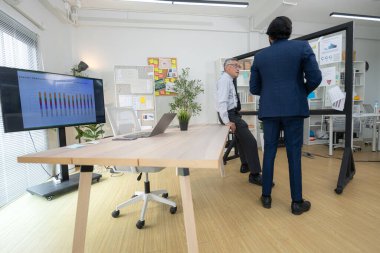 Çağdaş bir ofiste, iki üst düzey yönetici bir iş projesinin ilerleyişini izlemek ve beyin fırtınası yapmak istiyor.