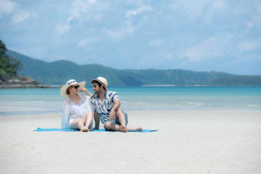 Genç çift beyaz kumlu sahilde tatil yapıyor, açık gökyüzü ve deniz.