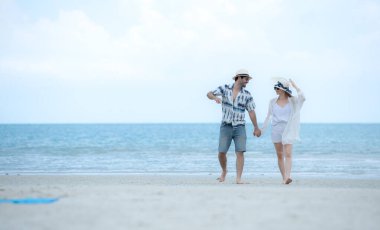 Genç çift beyaz kumlu sahilde tatil yapıyor, açık gökyüzü ve deniz.