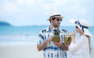 Genç çift beyaz kumlu sahilde tatil yapıyor, açık gökyüzü ve deniz.