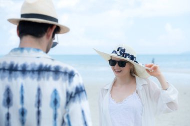 Genç çift beyaz kumlu sahilde tatil yapıyor, açık gökyüzü ve deniz.