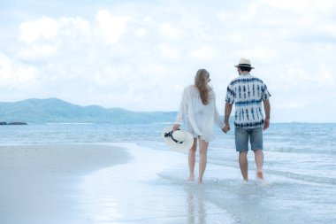 Genç çift beyaz kumlu sahilde tatil yapıyor, açık gökyüzü ve deniz.