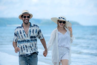 Genç çift beyaz kumlu sahilde tatil yapıyor, açık gökyüzü ve deniz.