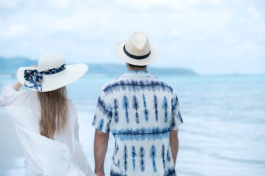 Genç çift beyaz kumlu sahilde tatil yapıyor, açık gökyüzü ve deniz.