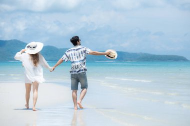 Genç çift beyaz kumlu sahilde tatil yapıyor, açık gökyüzü ve deniz.