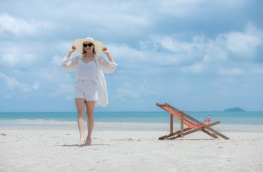 Genç bir kadın beyaz kumlu bir plajda, açık gökyüzünde ve denizde tatilde.