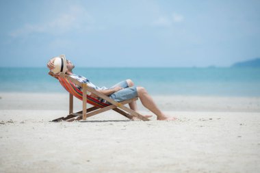 Genç adam beyaz kumlu sahilde tatilde, açık gökyüzü ve deniz