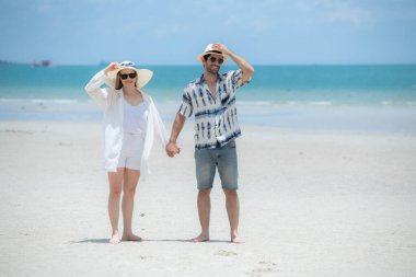 Genç çift beyaz kumlu sahilde tatil yapıyor, açık gökyüzü ve deniz.