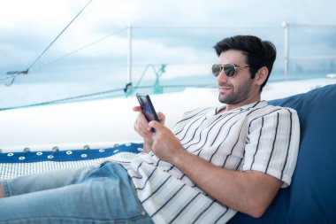 Genç bir adam deniz kenarındaki bir yatta eğleniyor.