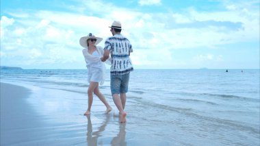 Genç çift beyaz kumlu sahilde tatil yapıyor, açık gökyüzü ve deniz.